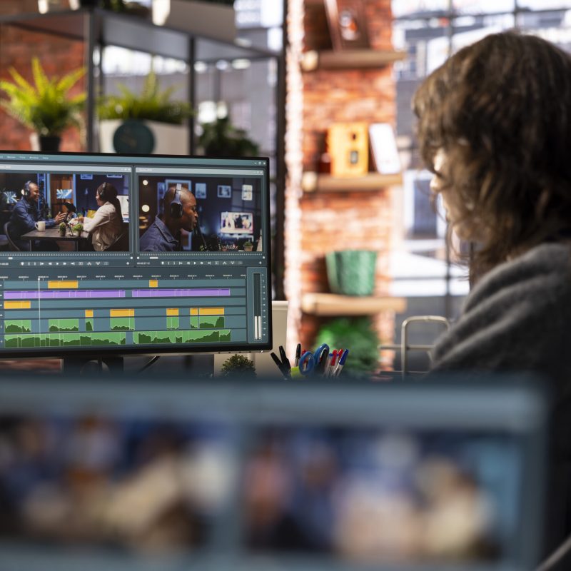 Female filmmaker working on media post production from agency office, ensuring the editing timeline and color correction for a video shoot. Tech driven workspace showcases a digital workflow.