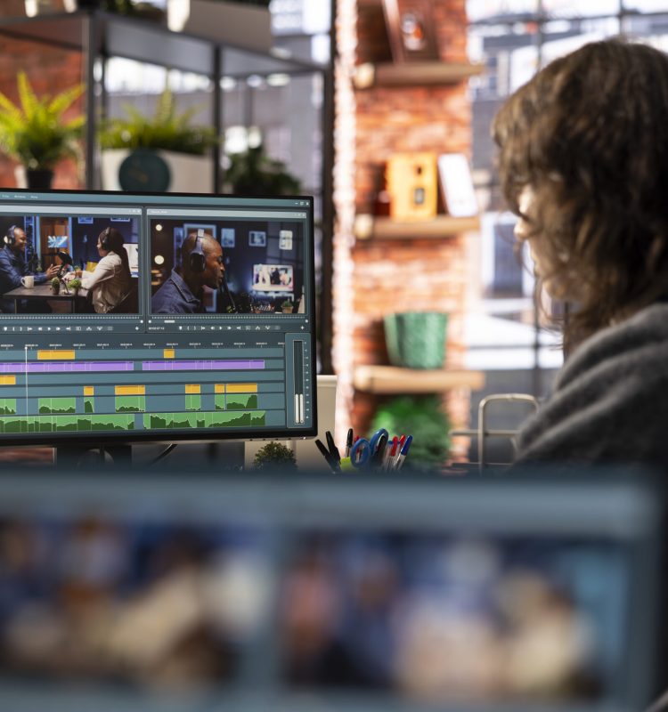 Female filmmaker working on media post production from agency office, ensuring the editing timeline and color correction for a video shoot. Tech driven workspace showcases a digital workflow.