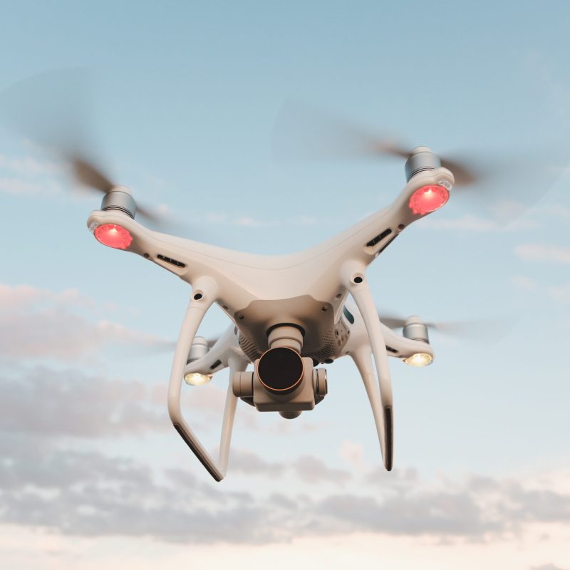 White drone hovering in a bright blue sky. Drone copter flying with digital camera